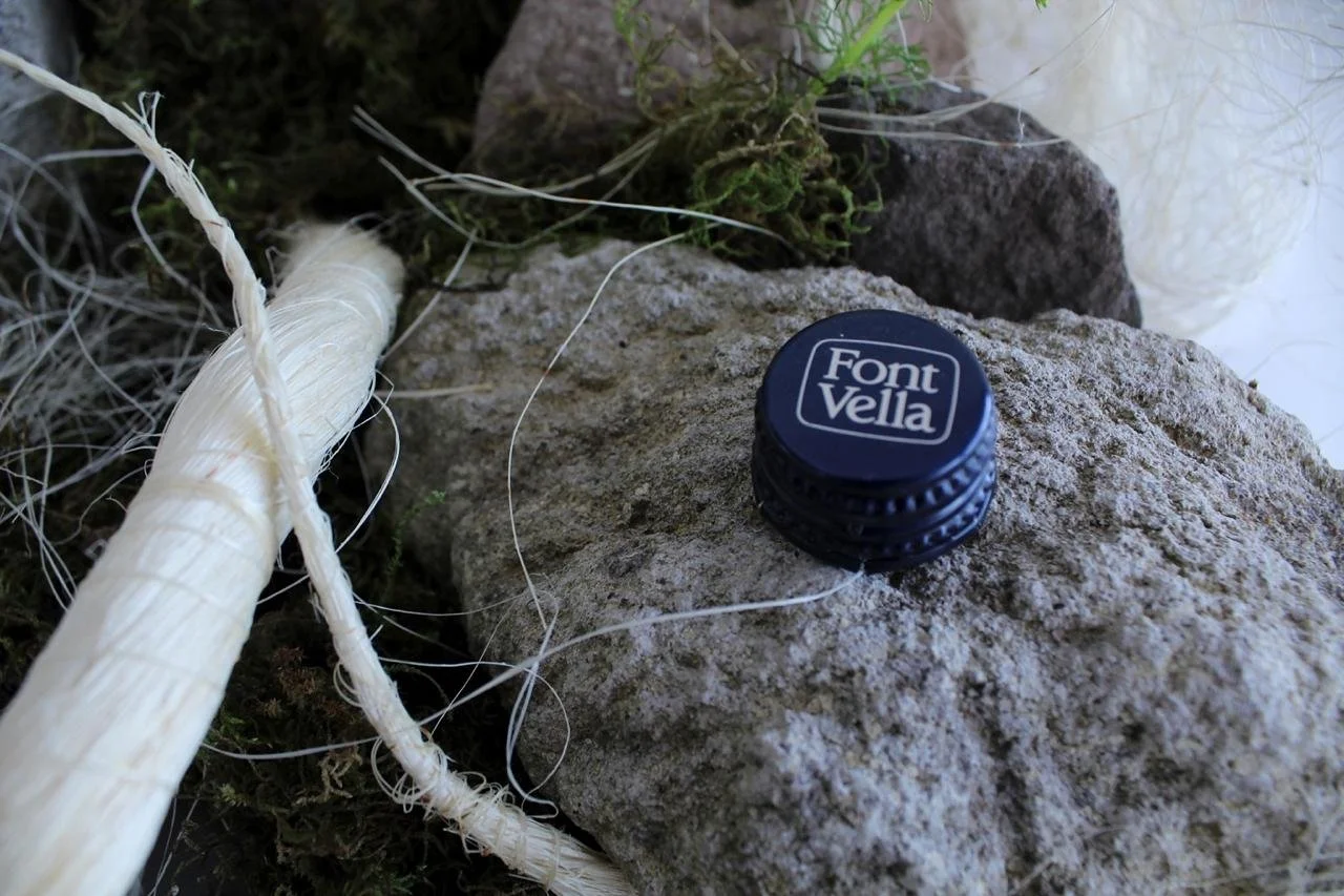 Close-up of a Font Vella bottle cap placed on rock and natural fibers as part of a contemporary floral installation by Ceci Bordas.