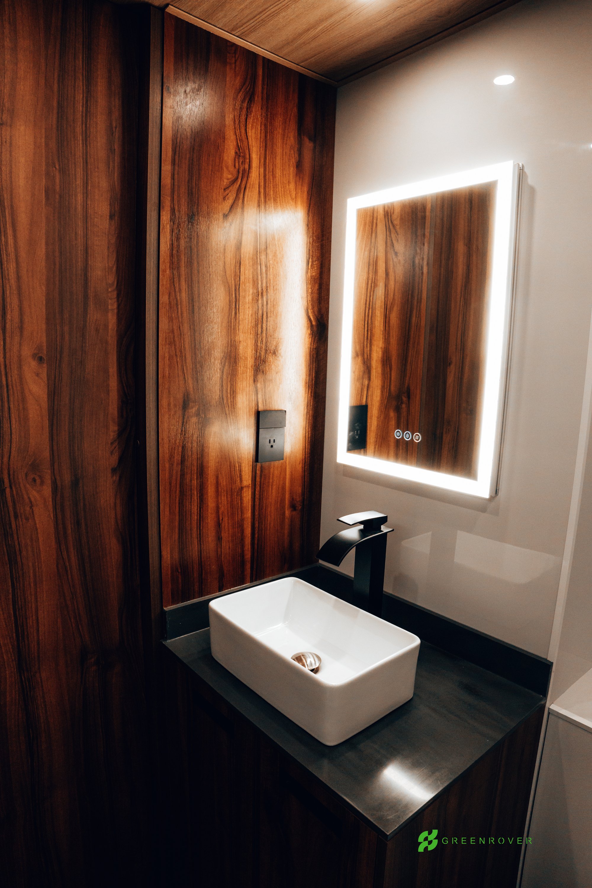 Modern bathroom with wooden wall, illuminated mirror, and white sink.
