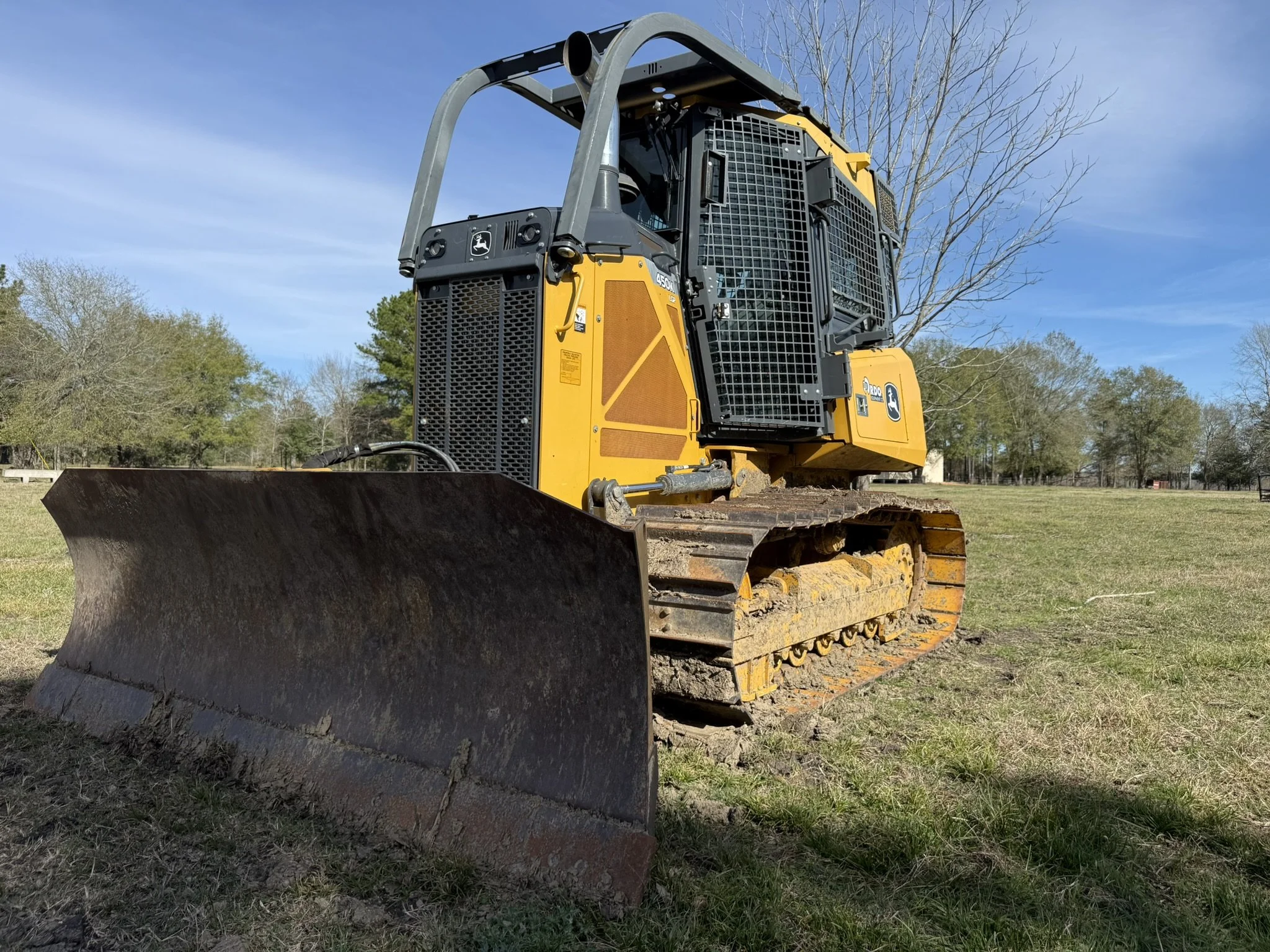 A yellow and black bulldozer parked on a grassy field with trees and a blue sky in the background.