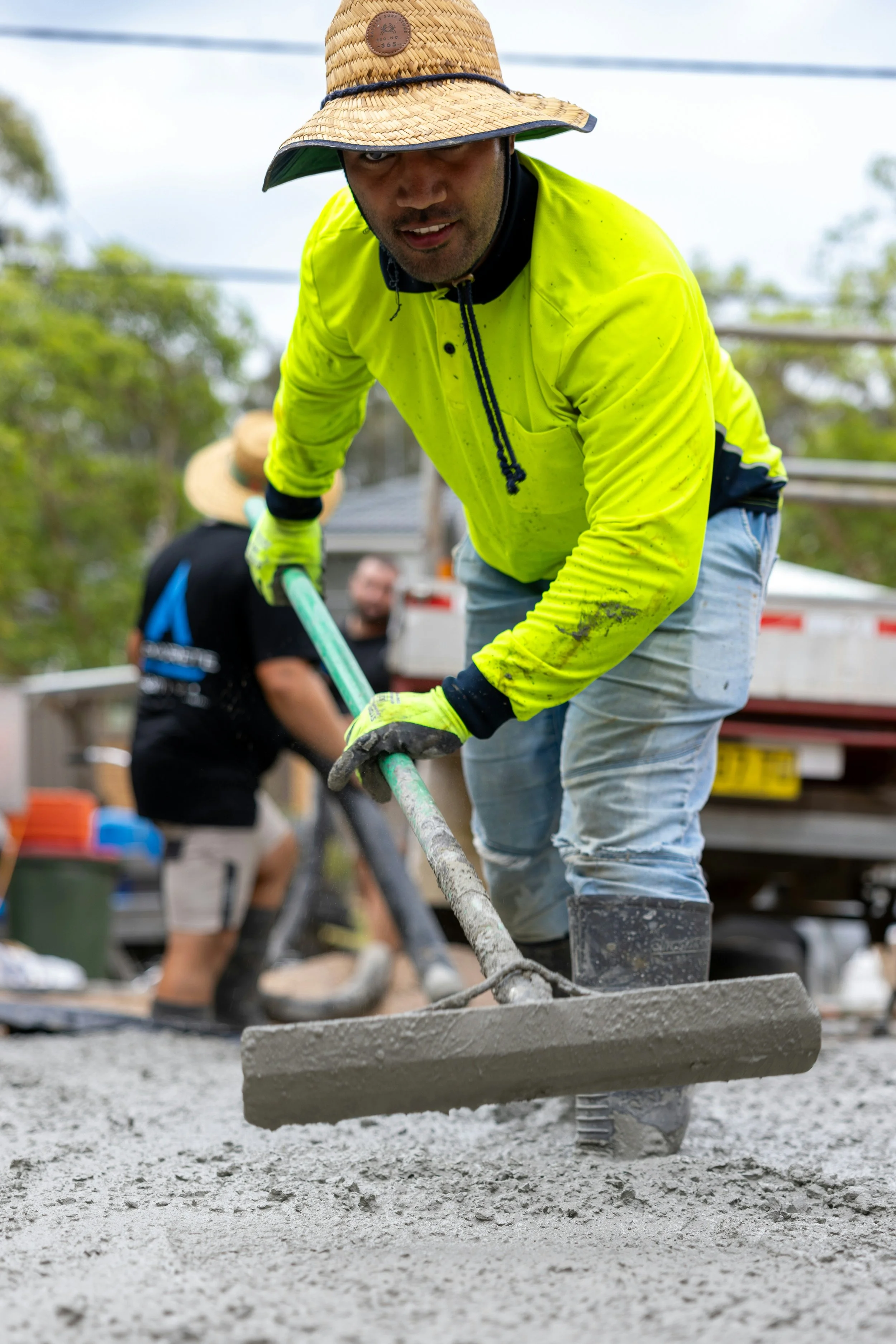 Construction worker in red hoodie and hard hat walking on a construction site with concrete forms and soil.