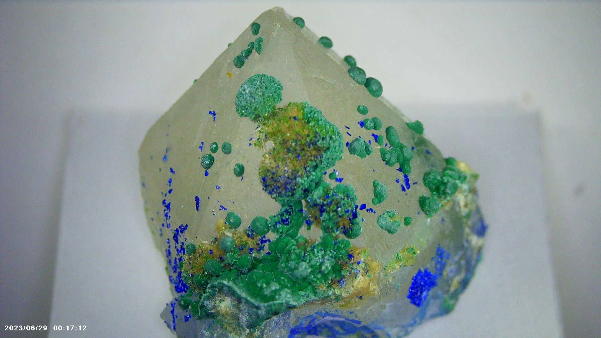 Close-up of a quartz crystal specimen with a diamond-shaped form, featuring green, blue, and yellow mineral coating and textures from Montana.