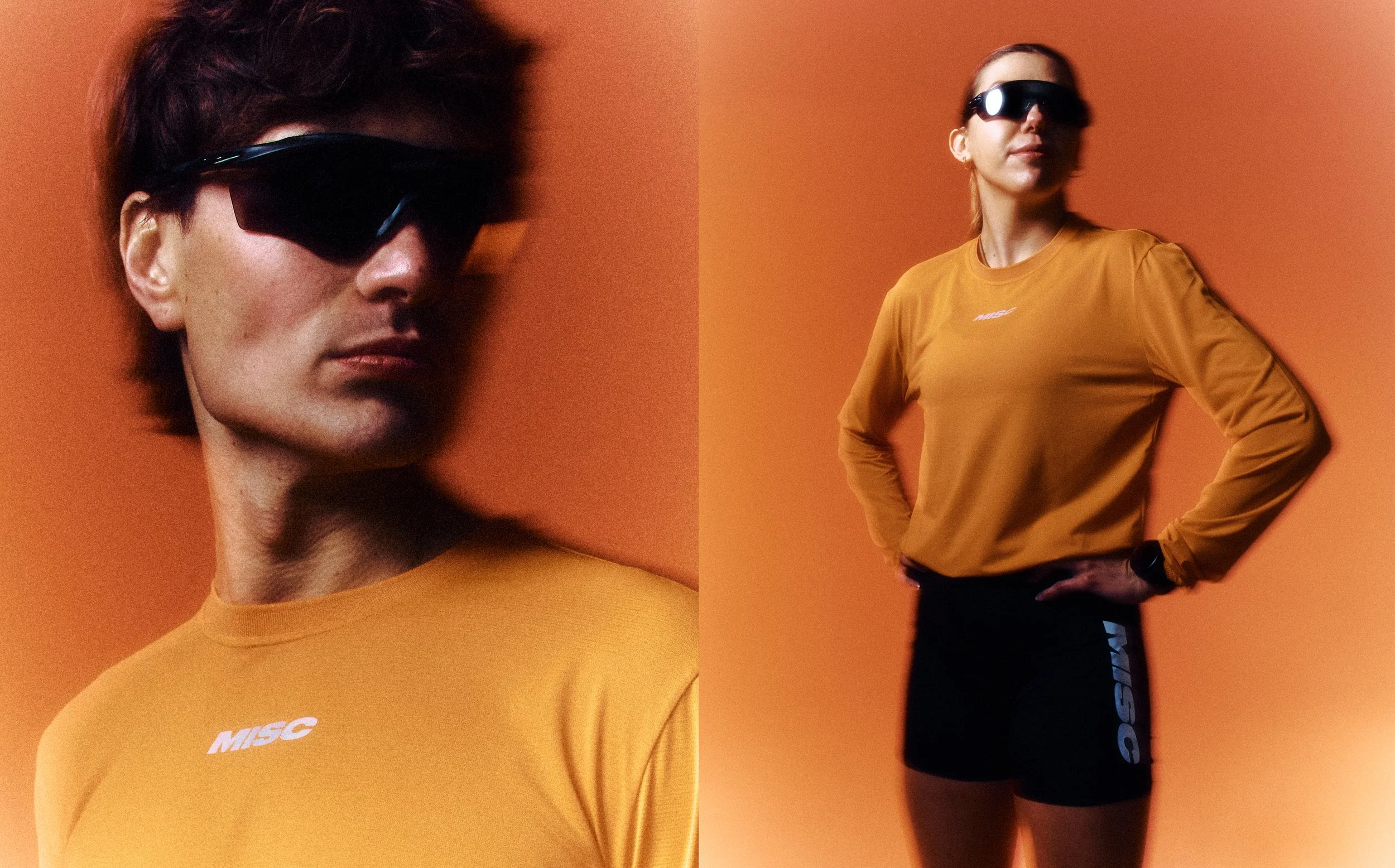 A woman wearing sunglasses, a mustard yellow long-sleeve shirt, and black athletic shorts, standing with one hand on her hip against an orange background.
