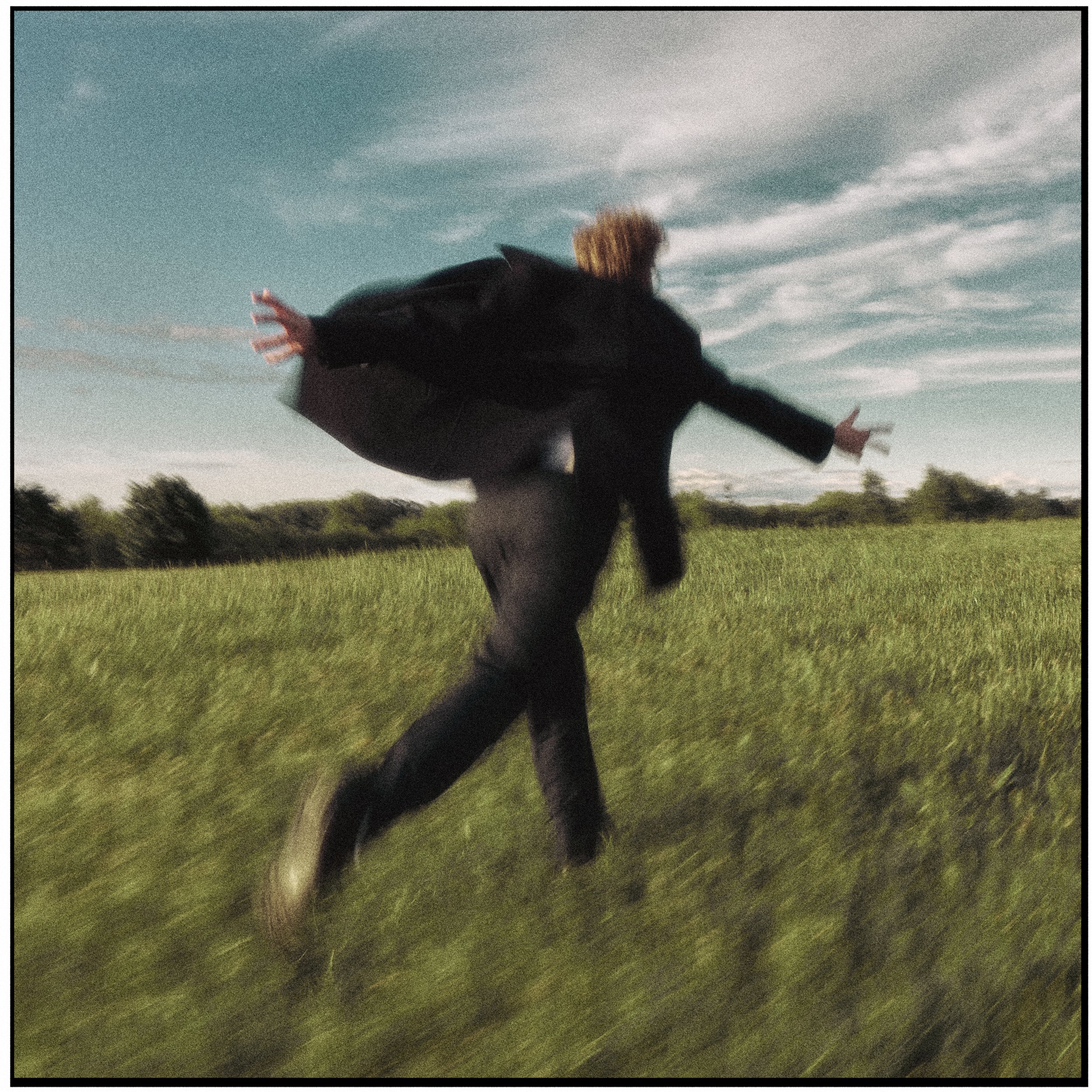 Person jumping in a grassy field with outstretched arms, under a partly cloudy sky.