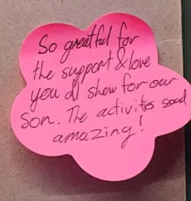 Pink flower-shaped sticky note with handwritten message expressing gratitude and love for support and showing for a son.