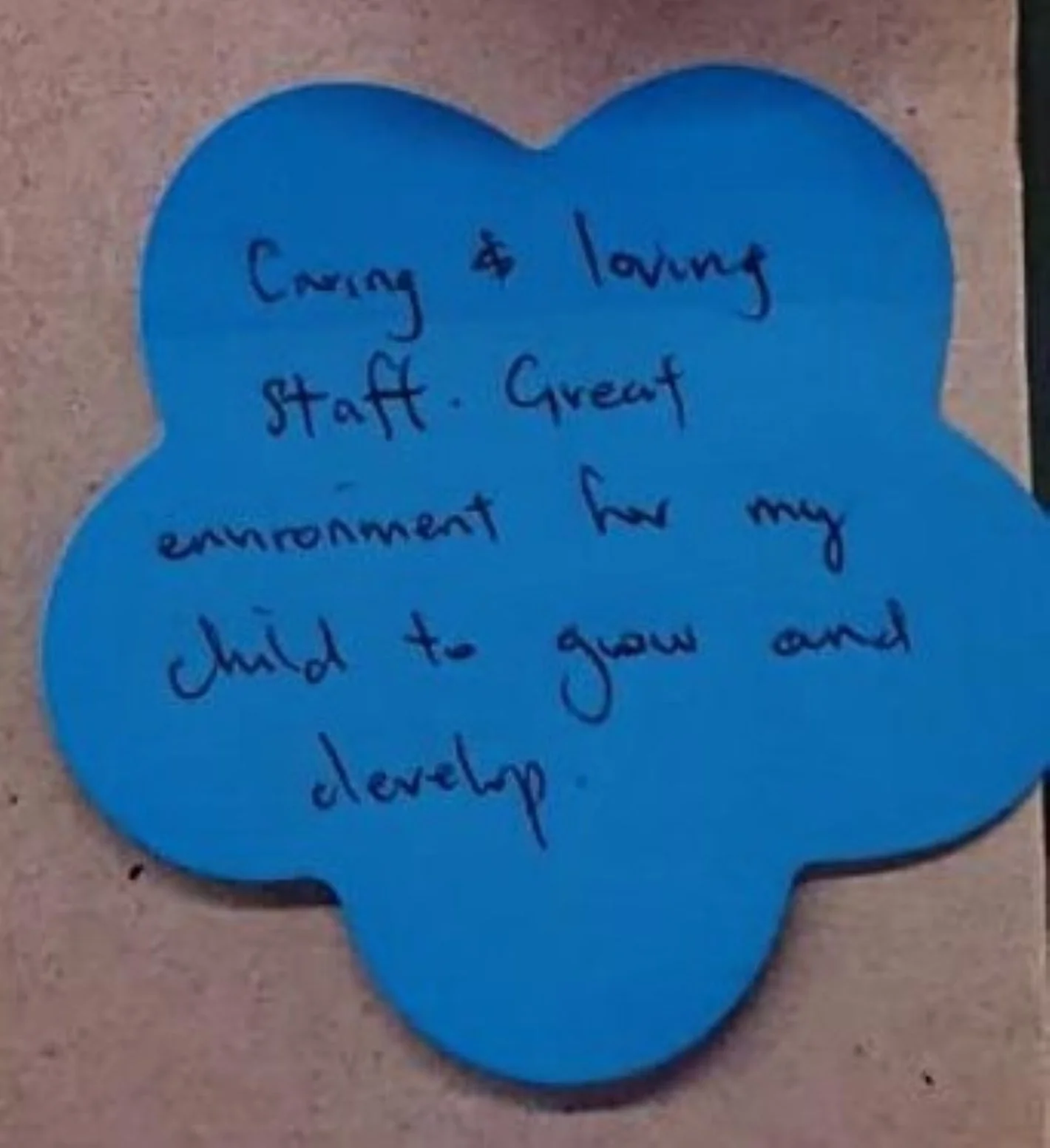 A blue paper in the shape of a flower with a parent's handwritten message in black ink about the caring and loving staff at St Mary's Children Centre, Kensington Victoria.