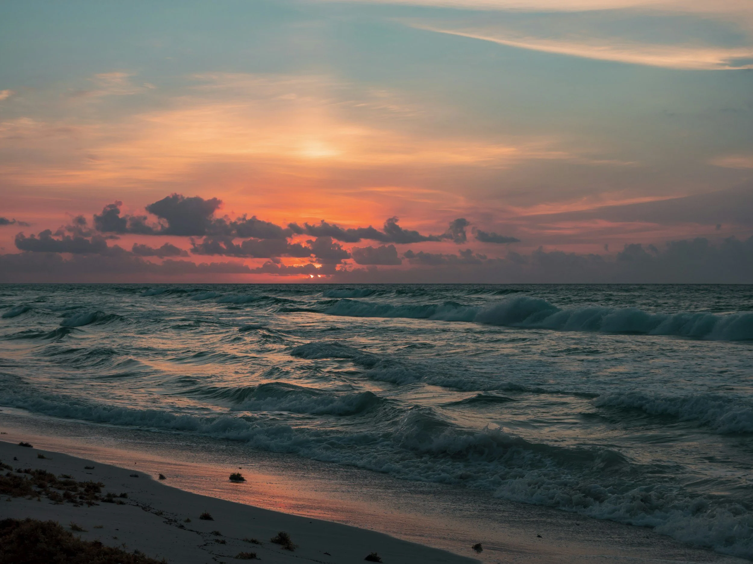 Sunset over the ocean with colorful sky and waves hitting the sandy beach.