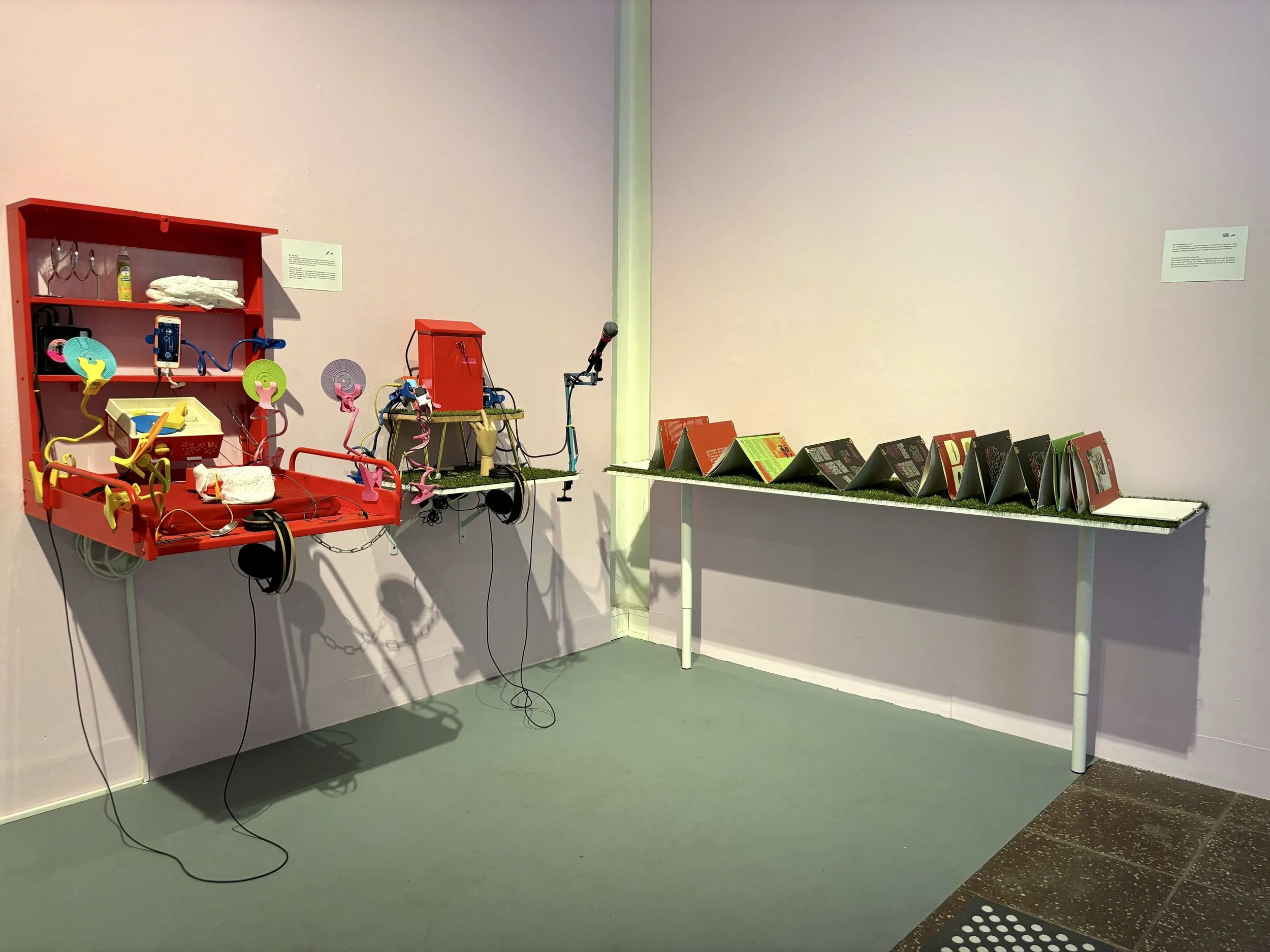 Ariel’s installation of a zine, a diaper station, and a mailbox featuring mini loudspeakers, a plastic turntable, and a chained hand mannequin. Photo: Jay Afrisando. Event: “In Conversation” exhibition, 2025.