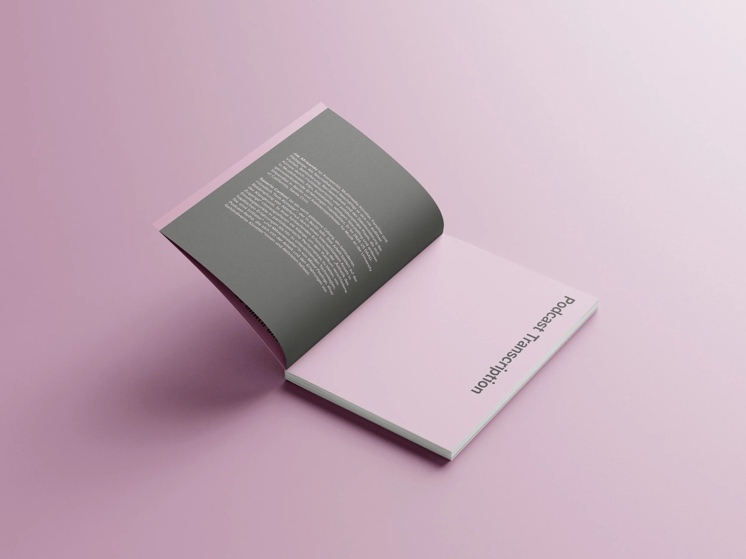 An opened transcript book, showing pink text on a dark grey page and dark grey text on a pink background, photographed in a studio on a pink surface. Photo: Lai Guim.
