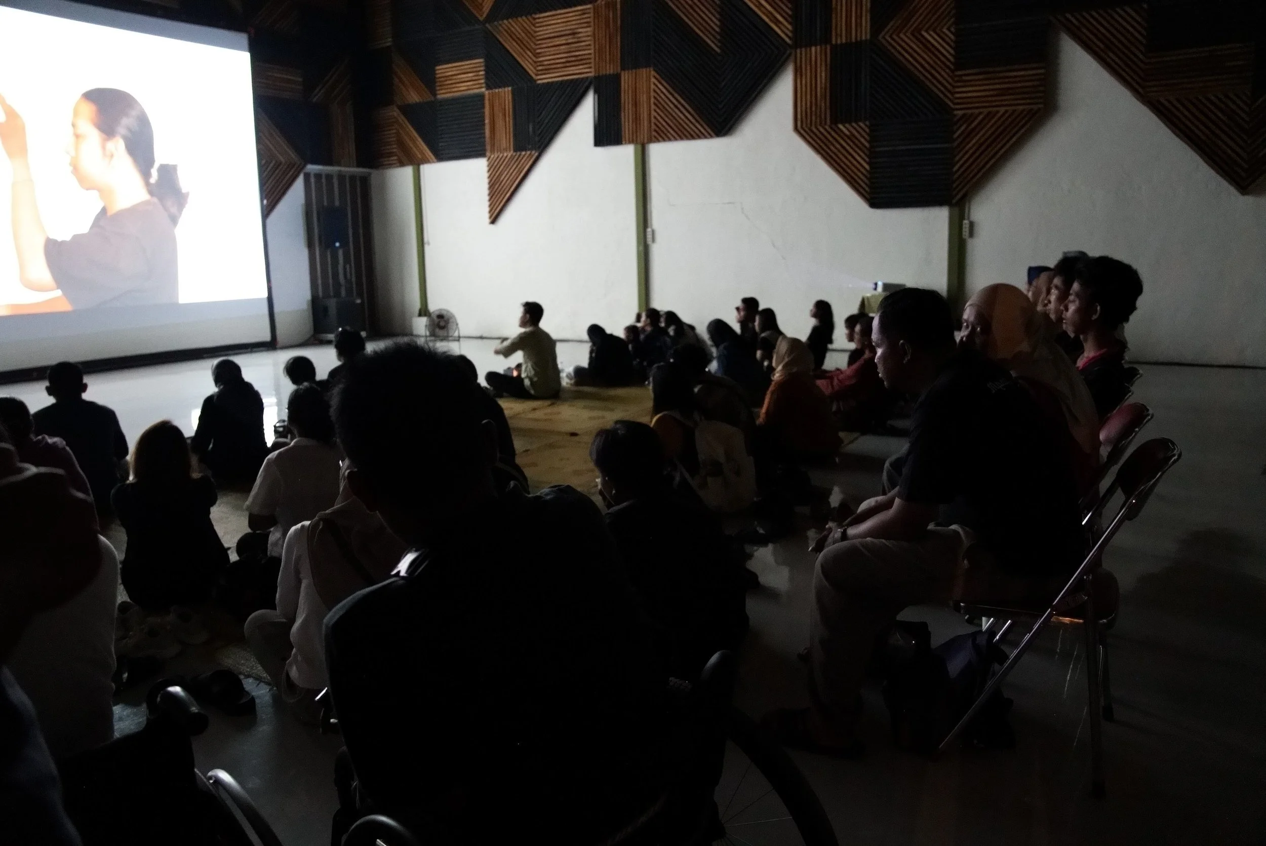 A seated audience, mostly on a floor mat, watching the film. Photo: Singgih Baruna. Event: Screening at Padepokan Seni Bagong Kussudiardja, 2025.