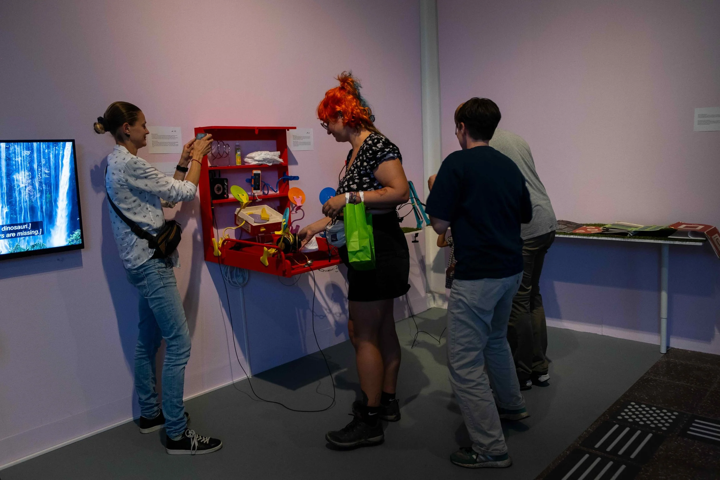 Four visitors are accessing an installation of a diaper station and a self-made mailbox. Photo: Mareike J. Lange. Event: “In Conversation” exhibition, 2025.