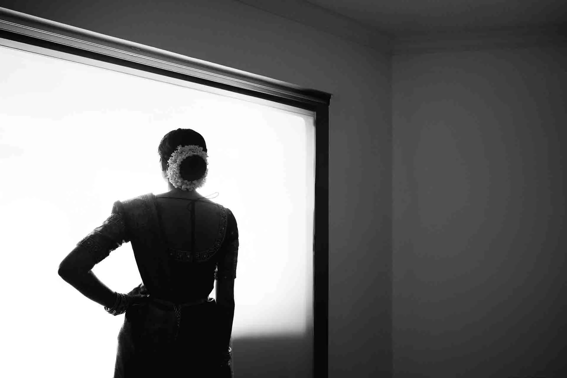 Silhouette of a woman in traditional Mexican dress standing in front of a bright, backlit window, with her hand on her hip.
