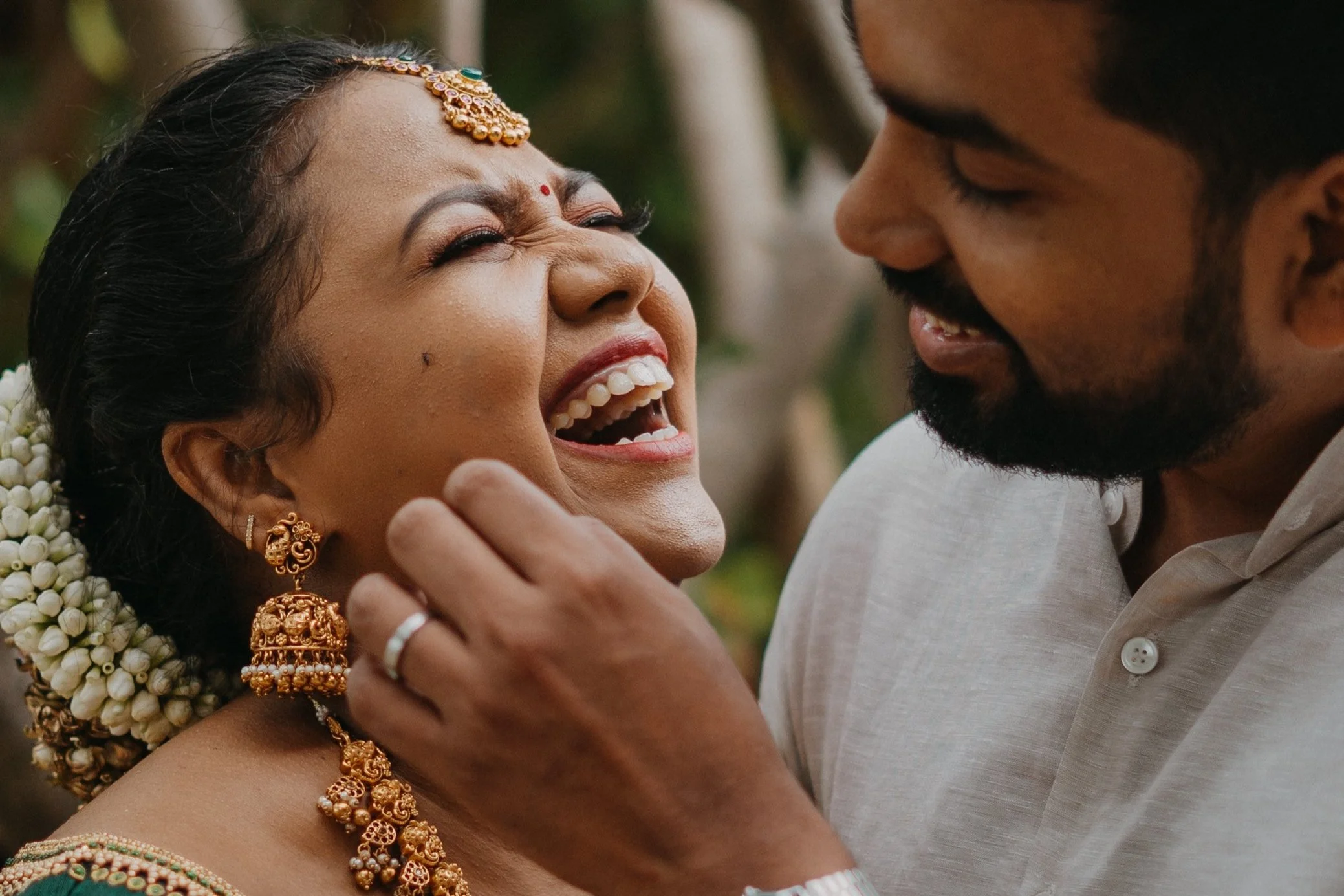 A man and a woman sharing a joyful moment, with the woman laughing and the man smiling, in an outdoor setting.