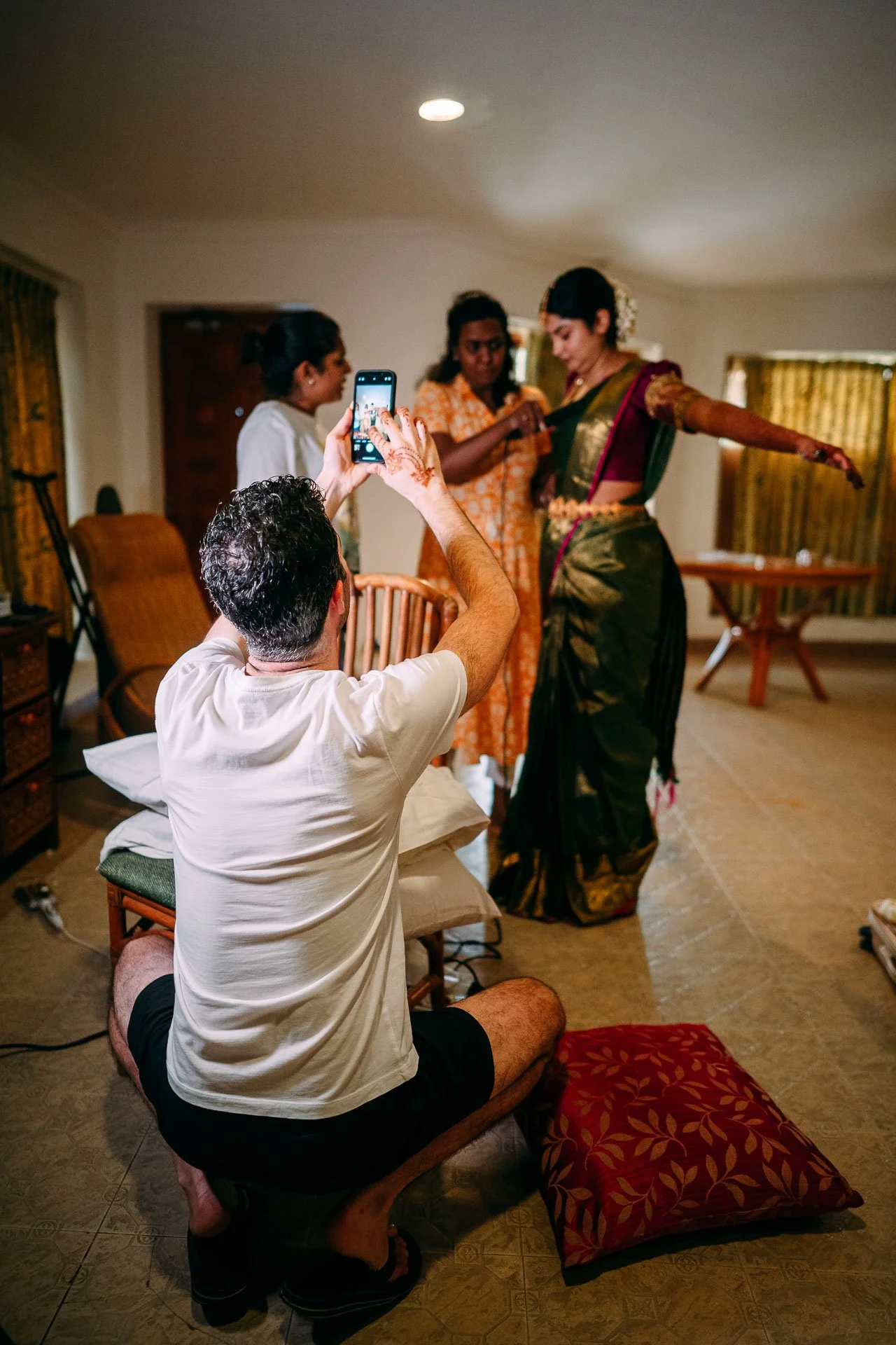 A man taking a photo of three women in traditional Indian attire inside a home.