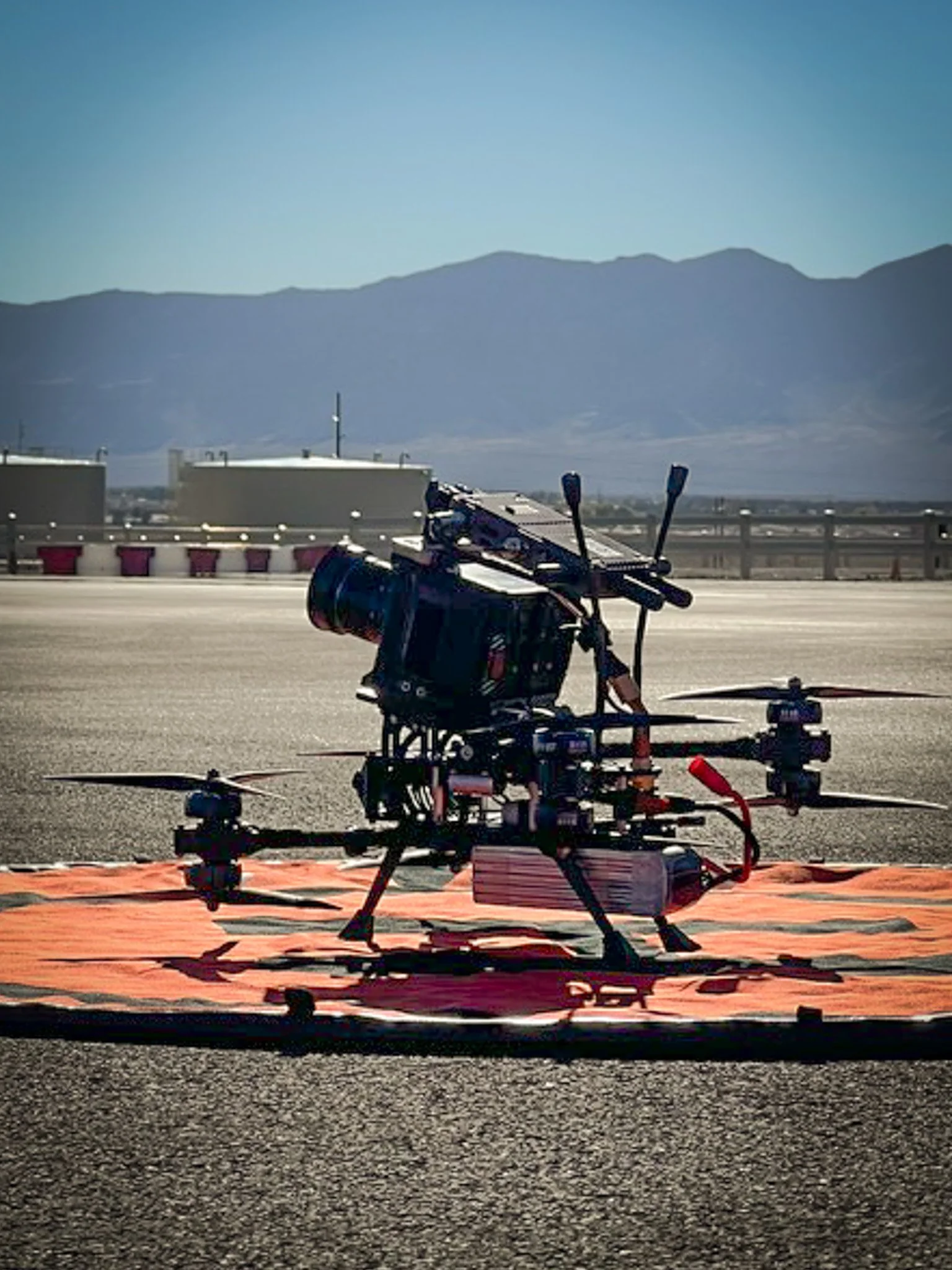 A drone with a camera attached, placed on an orange mat on a road with mountains in the background.