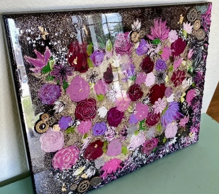 A glass art piece with various pink, purple, and red roses, butterflies, and abstract designs, placed on a green surface near a wall.