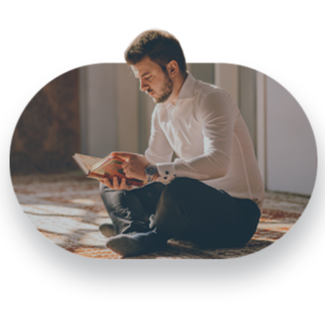 Man sitting cross-legged on a rug reading a book indoors
