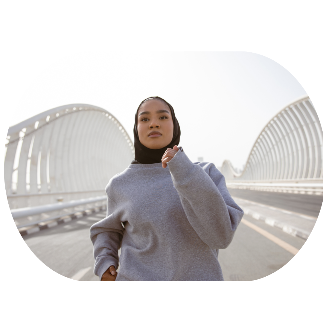 Person wearing a gray sweatshirt and black hijab jogging on a modern bridge with white architectural elements.