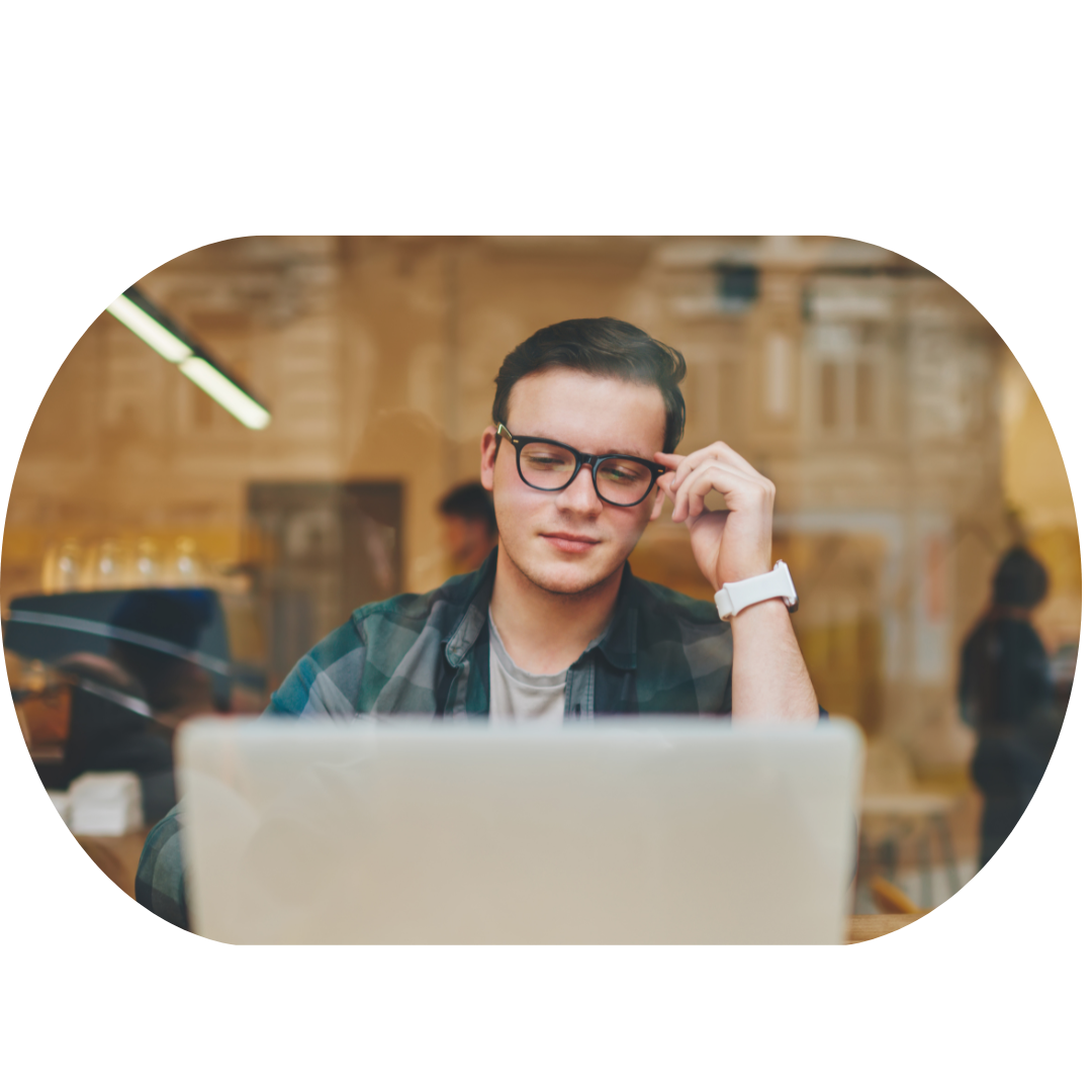 Person wearing glasses using a laptop in a cozy cafe setting, with reflections on the window.