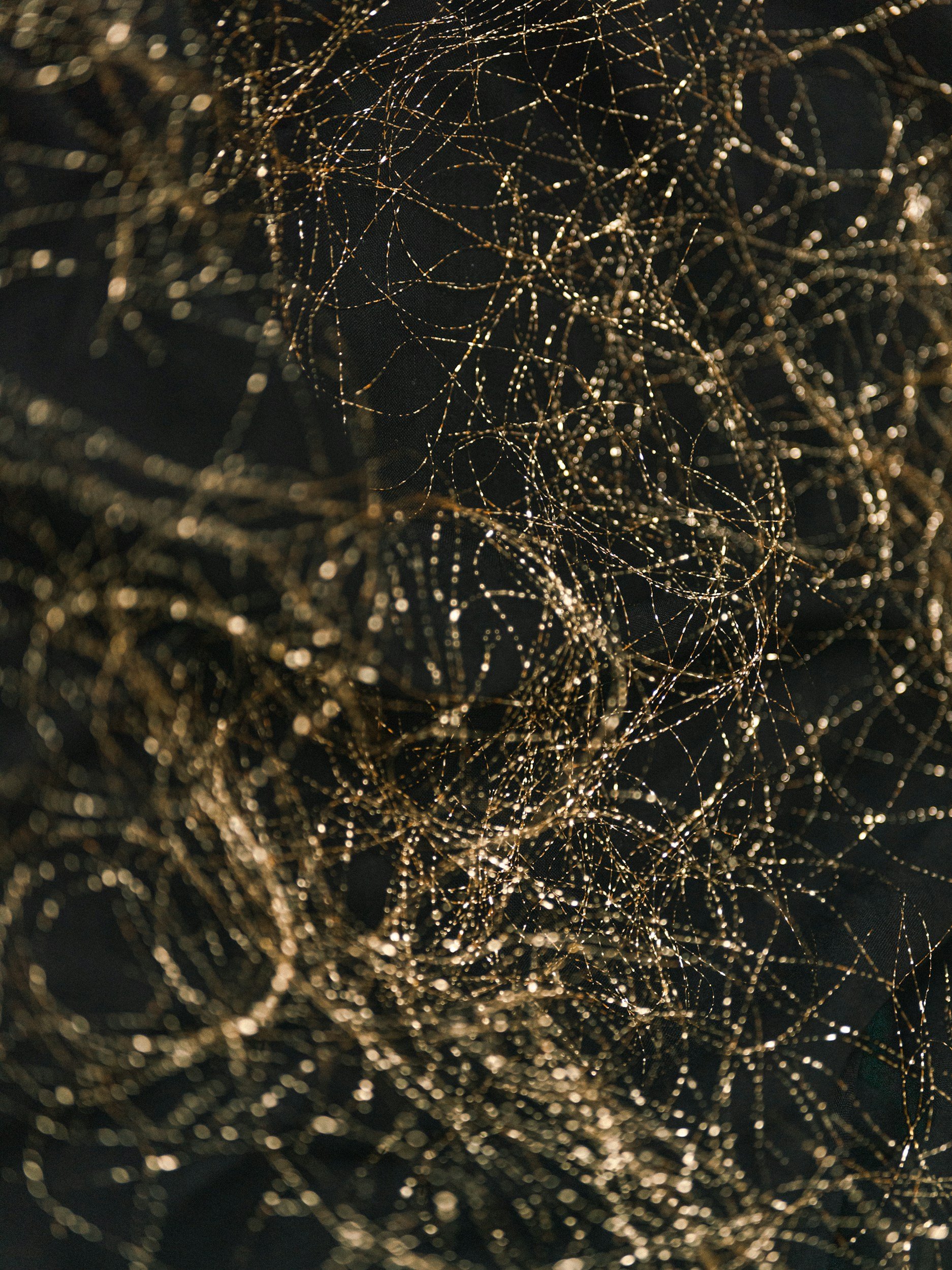 A close-up of tangled gold thread with small sparkling beads on a black background.