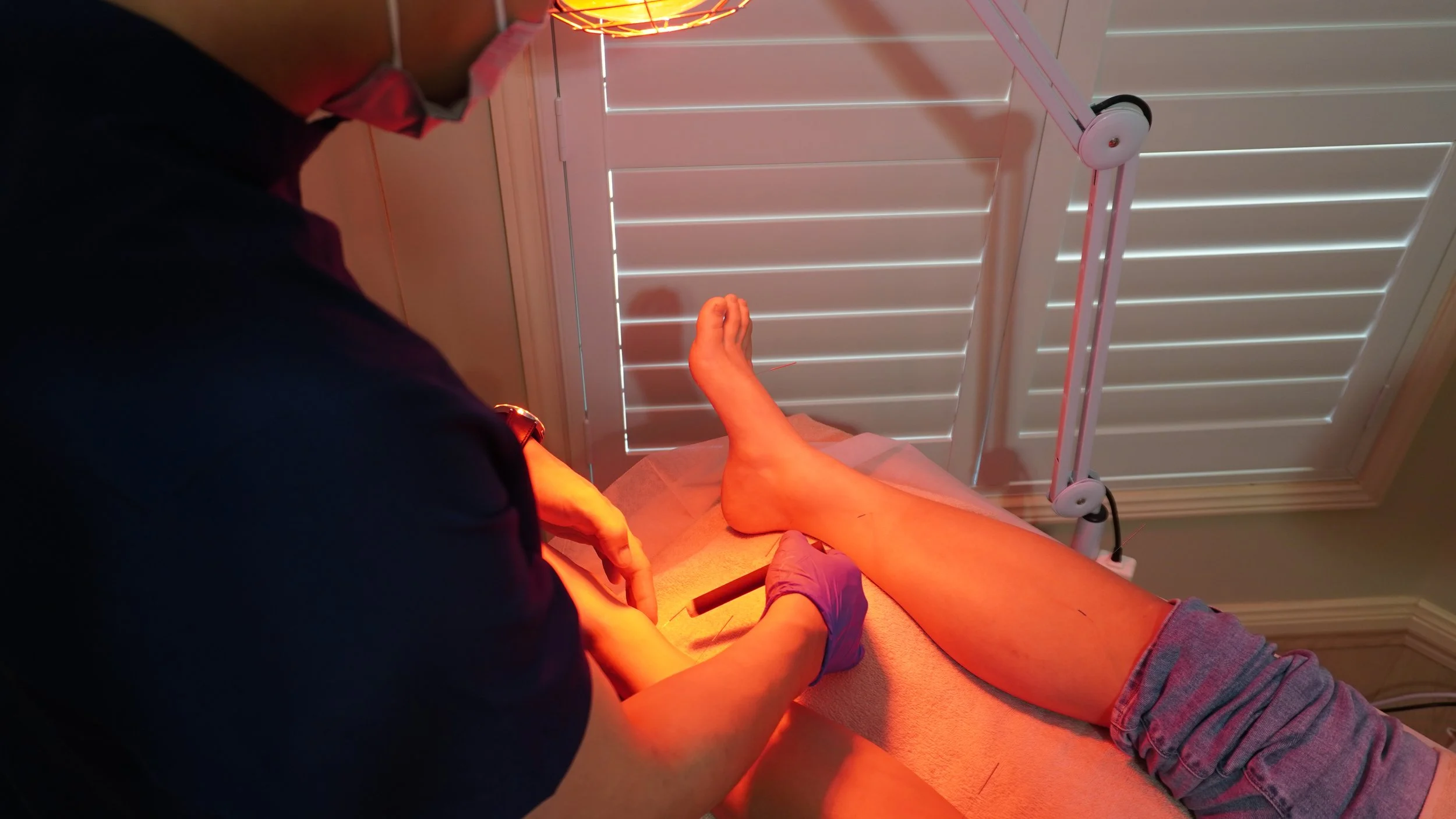 A person lying on a medical examination table with their leg elevated, receiving a treatment from a healthcare professional in a clinical setting.