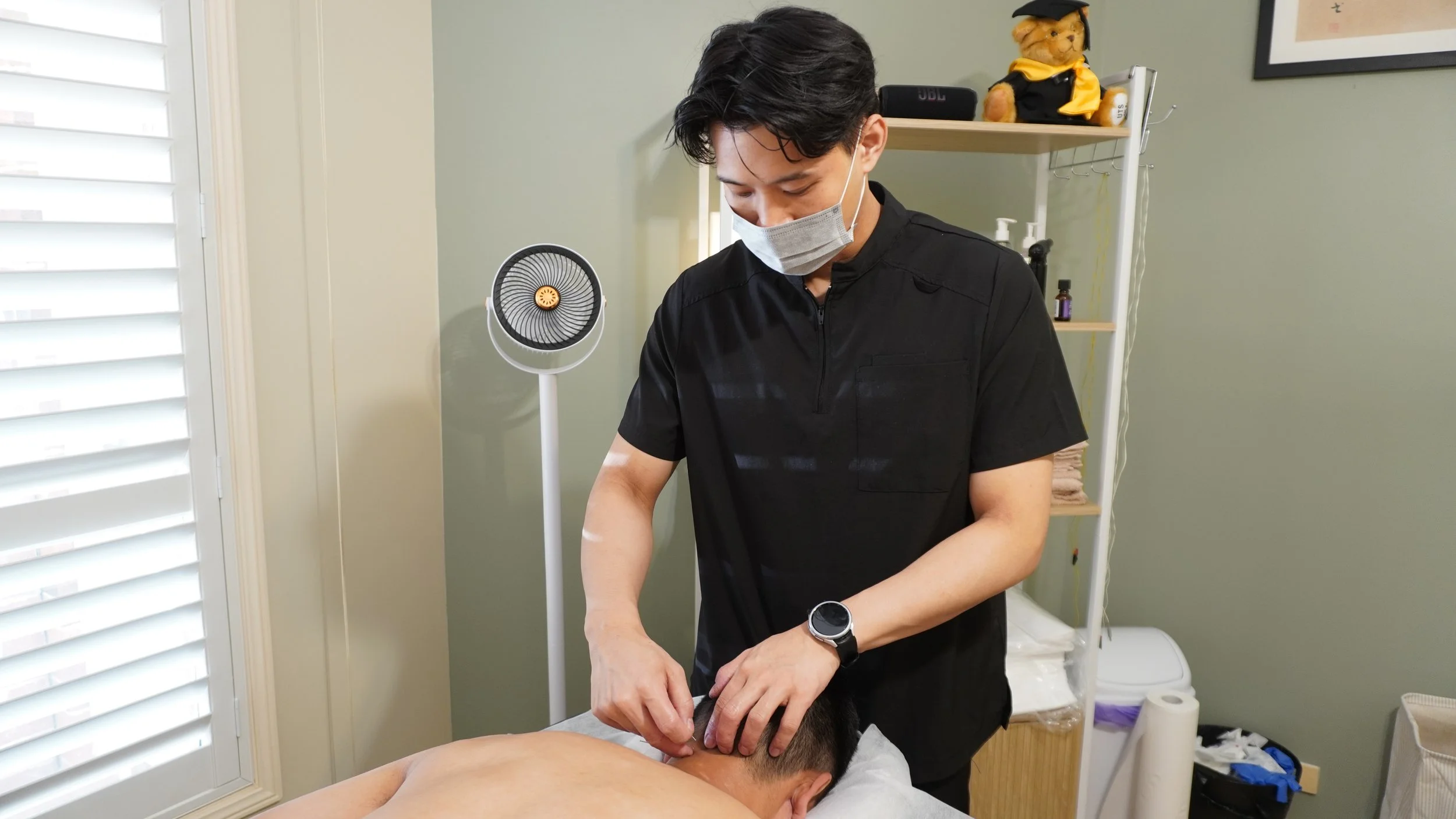 A man giving a massage to a person lying face down on a treatment table in a massage or therapy room.