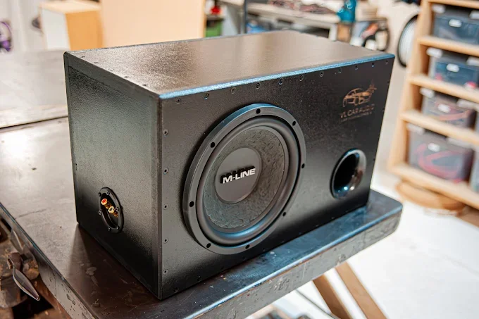 Un caisson de basse noir avec un grand haut-parleur et une entrée audio RCA, placé sur une table de travail.