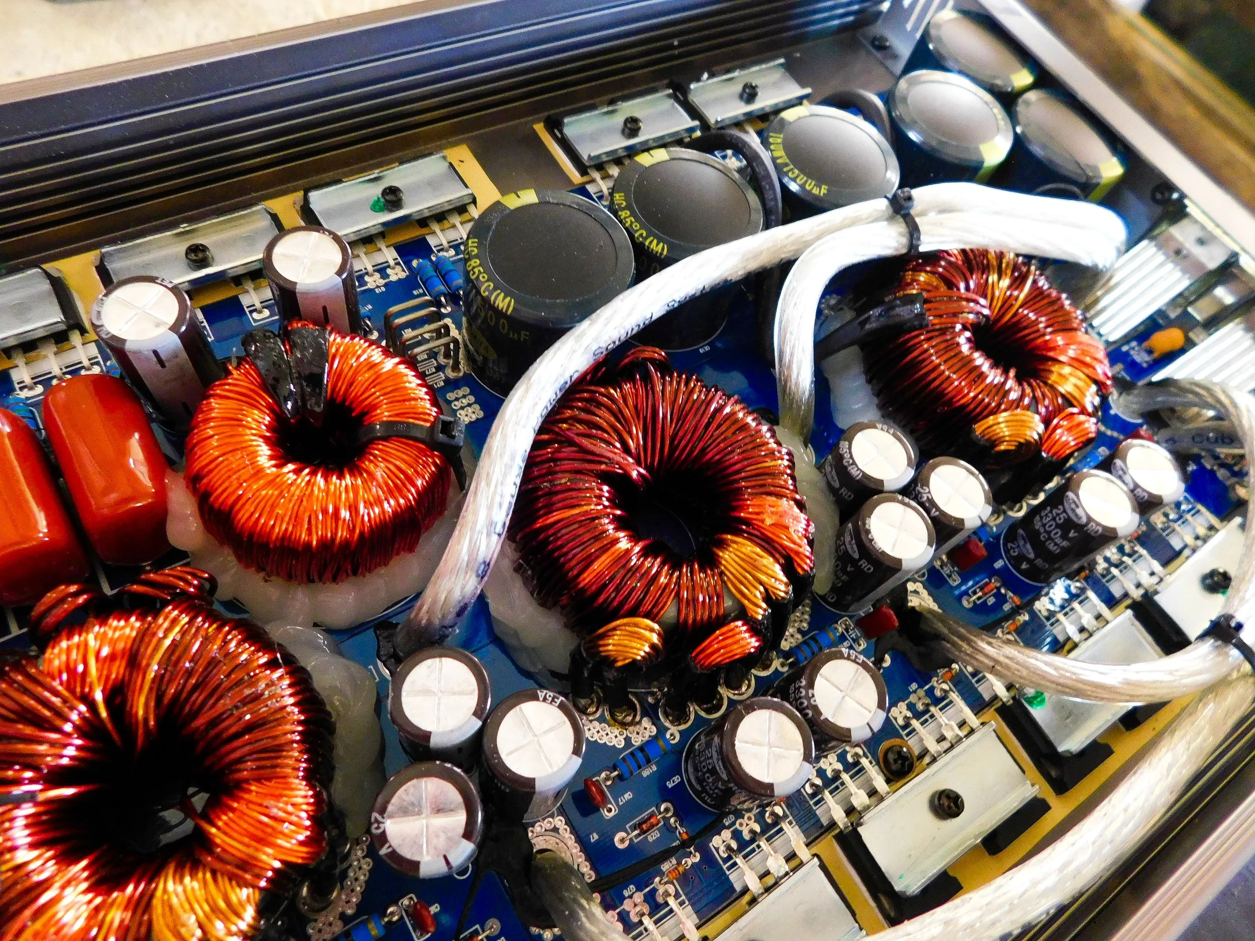 Détail d'un circuit électronique avec des bobines de cuivre, des condensateurs, des résistances, des câbles et d'autres composants électroniques.