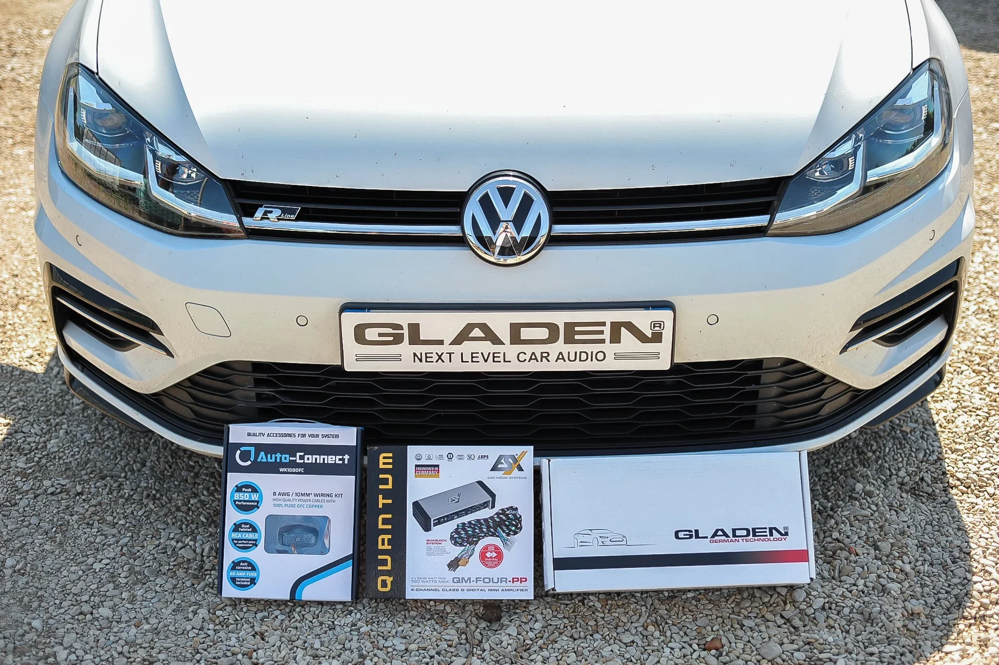 Une voiture blanche, un Volkswagen, avec des équipements de son et de mise à niveau audio posés devant elle sur un sol en gravier.