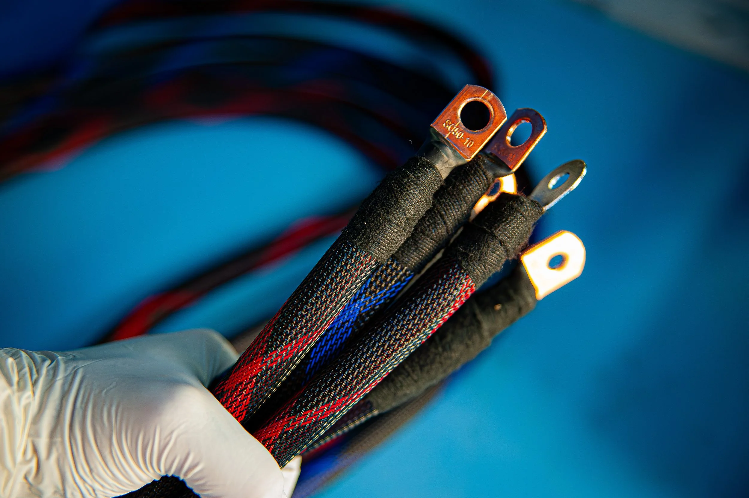 Câbles électriques avec terminaux en cuivre, tenus par une main portant un gant en latex, fond bleu.