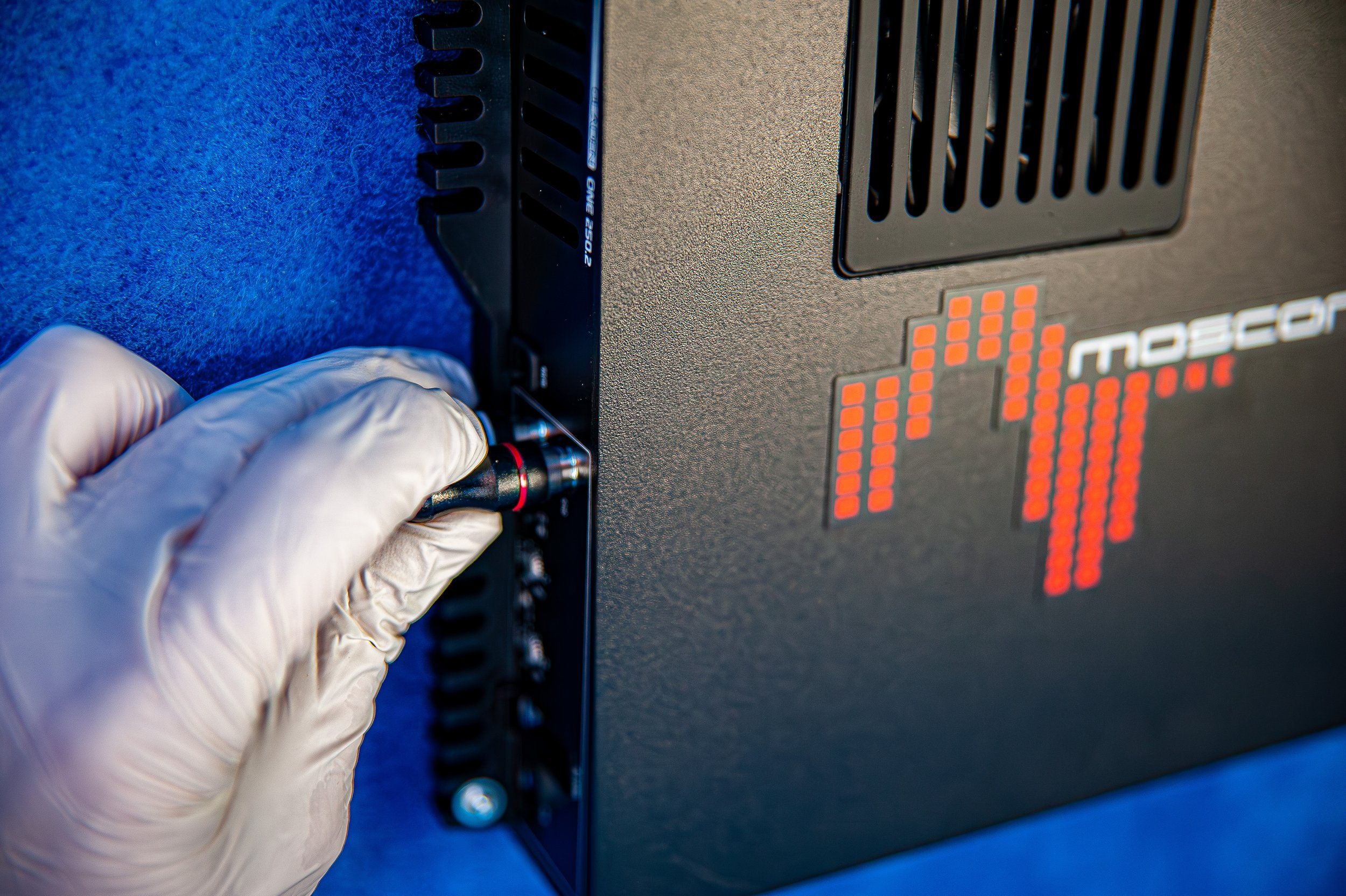 Une main gantée insère un câble dans une unité informatique ou un serveur, avec un fond bleu et un logo numérique lumineux.