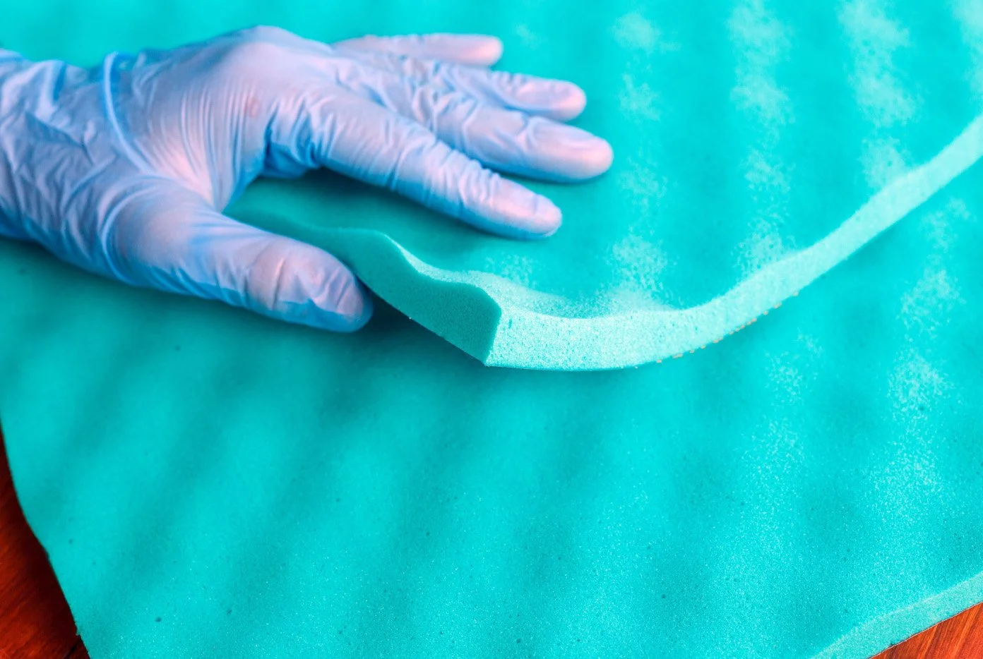 Une main portant un gant de procédé en caoutchouc turquoise manipule une grande plaque de mousse de couleur turquoise.