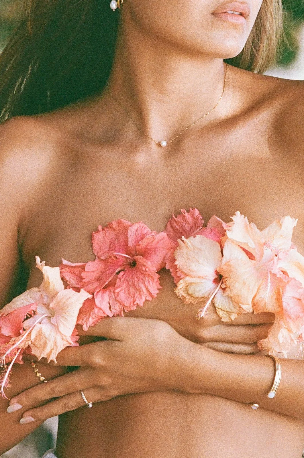 Close-up van een vrouw met bloemen op haar borst, sieraden en een lichte huid.