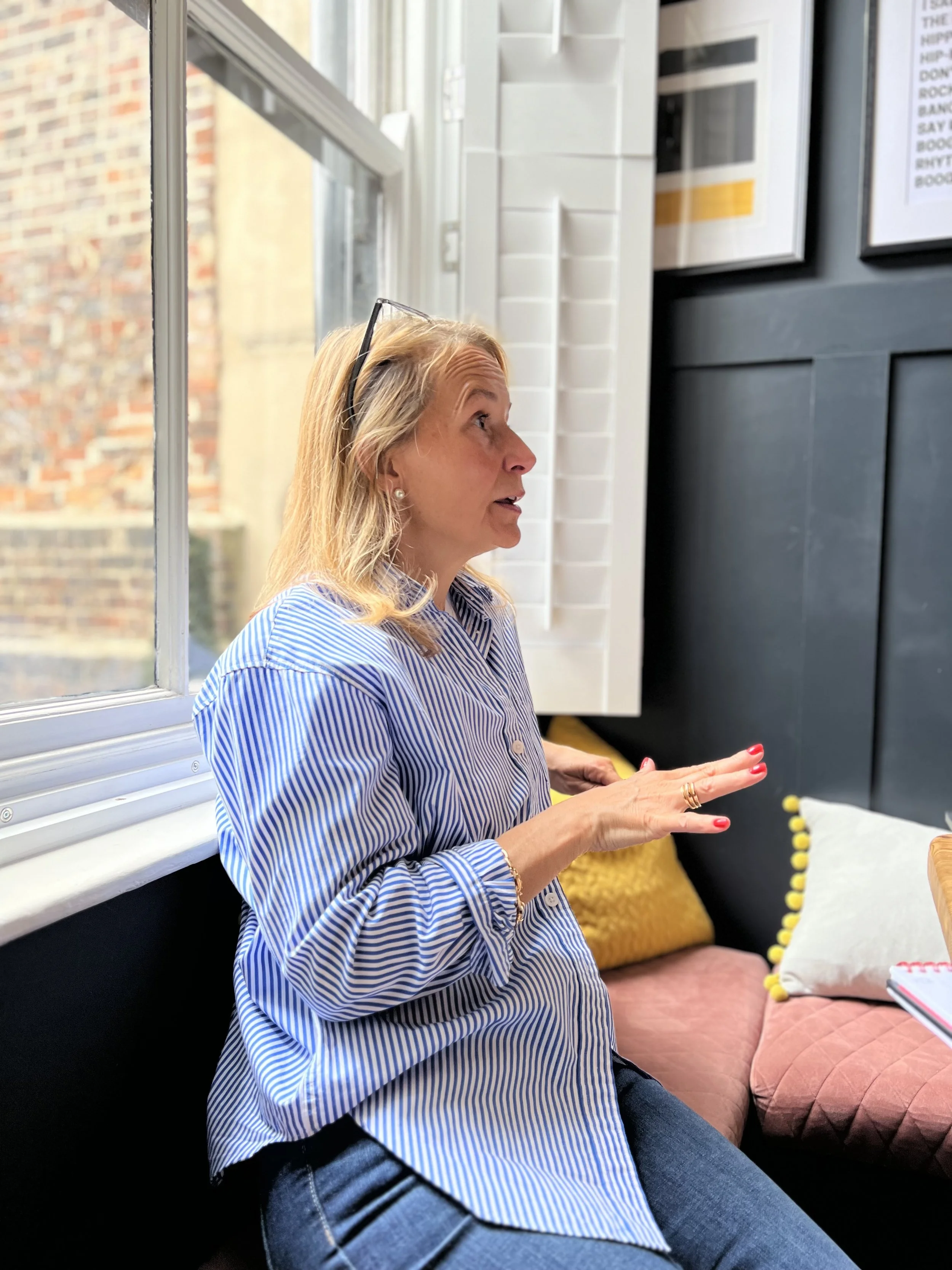Joanna Taylor, co-founder of Le Pub Scientifique, speaking during a discussion on pain education and clinician development, seated by a window in a relaxed setting.