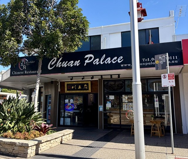Exterior of a Chinese restaurant called 'Chuan Palace' on a sunny day showing a large decorative brick garden planter box out the front, some tables and chairs and decorative motifs on the building.