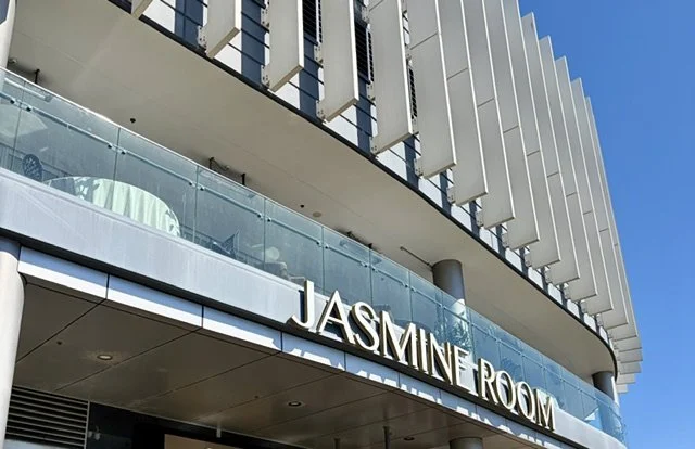 View looking up to terrace with glass balcony and large neon signage for the Jasmine Room Chinese restaurant in Southport on a clear blue sky day background.