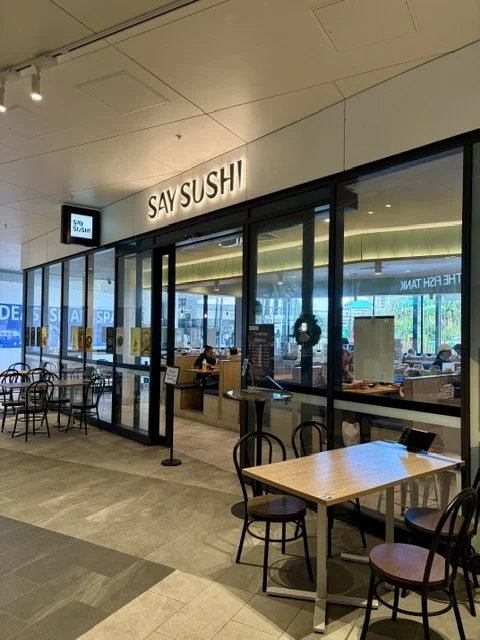 The exterior of 'Say Sushi' Japanese restaurant in Southport showing the front entry with illuminated signage above, and tables and chairs at the front.