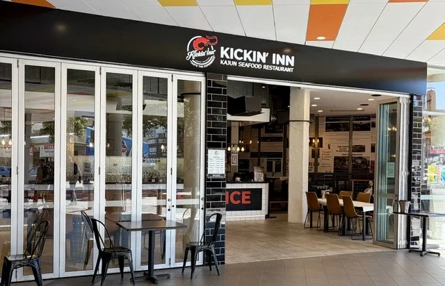 Front entrance of seafood restaurant called 'Kickin Inn', modern shopfront with concertina glass and steel doors and tables and chairs out the front.