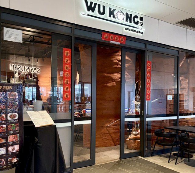 Outside view of Chinese restaurant WU KONG Kitchen & Bar with red cloth Chinese symbols either side of the front doors and Wu Kong illuminated signage above.