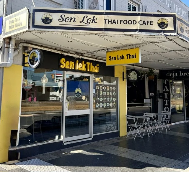 Street view of Sen Lek Thai Food Cafe in Southport with bright yellow walls and large signage above doors and on street awning, also some white tables and chairs out front.