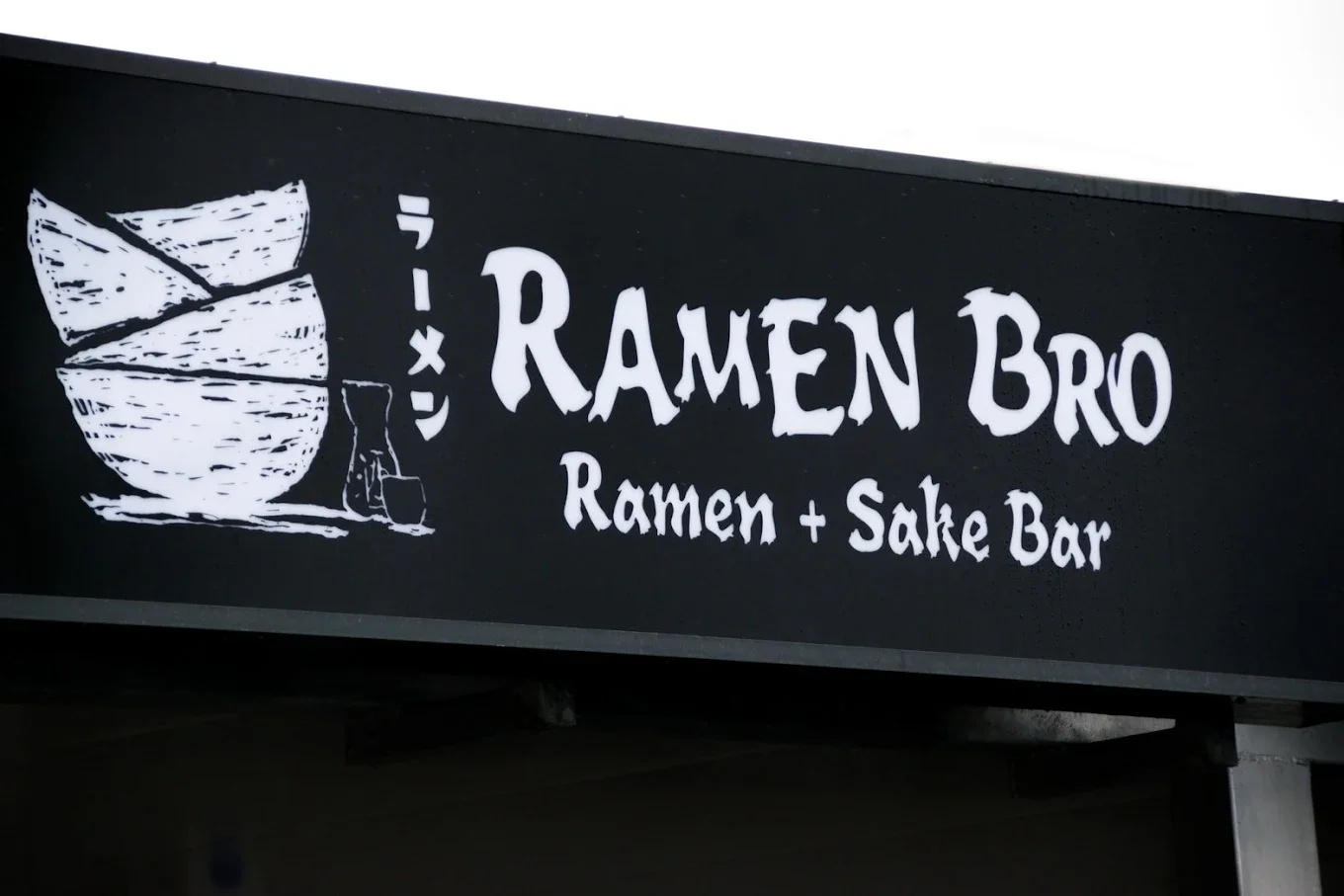 Sign for Ramen Bro, a ramen and sake bar, with a drawing of ramen bowls and a sake bottle.