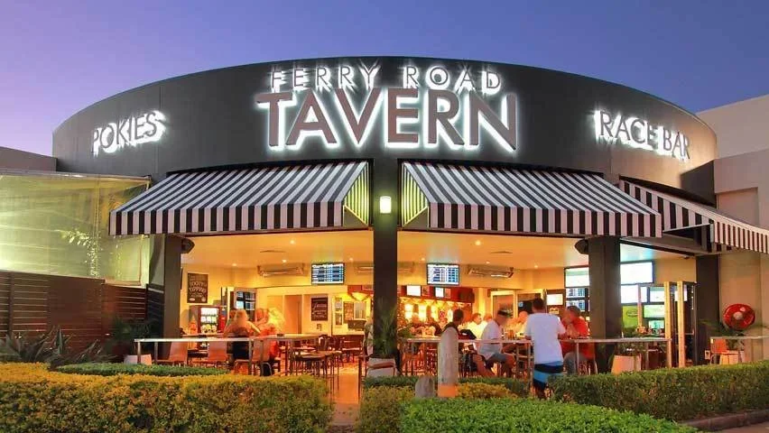 Outside view of the Ferry Road Tavern, showing a lit sign with neon lights, striped awnings, outdoor seating area, and people dining inside.
