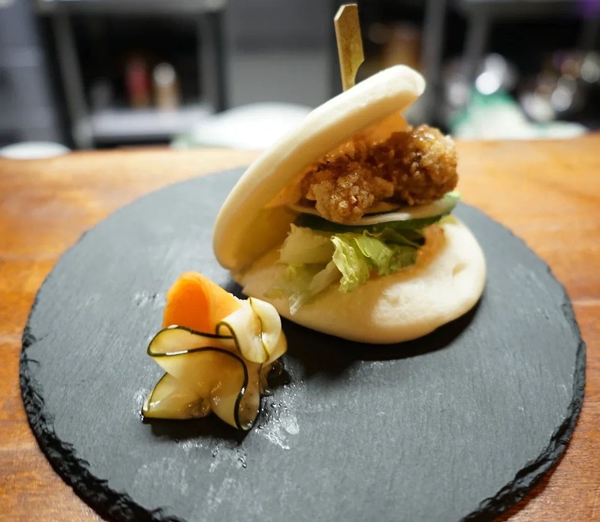 Chicken in a steamed bun, served with pickled vegetables on a black slate platter.