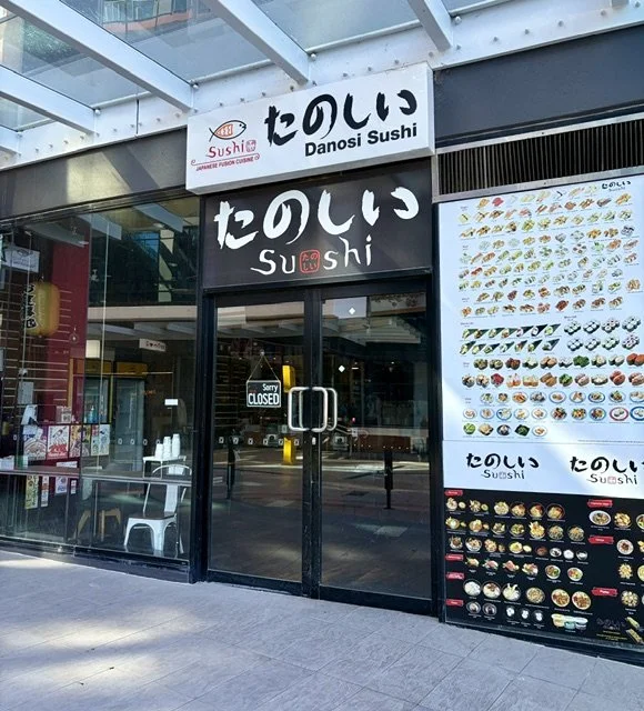 Front view of Japanese restaurant 'Danosi Kitchen' in Southport with black white and red light-box signage and a large display of various sushi on one window.