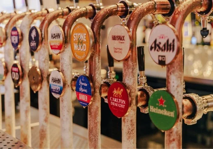 Beer tap handles from various breweries lined up on a bar counter.