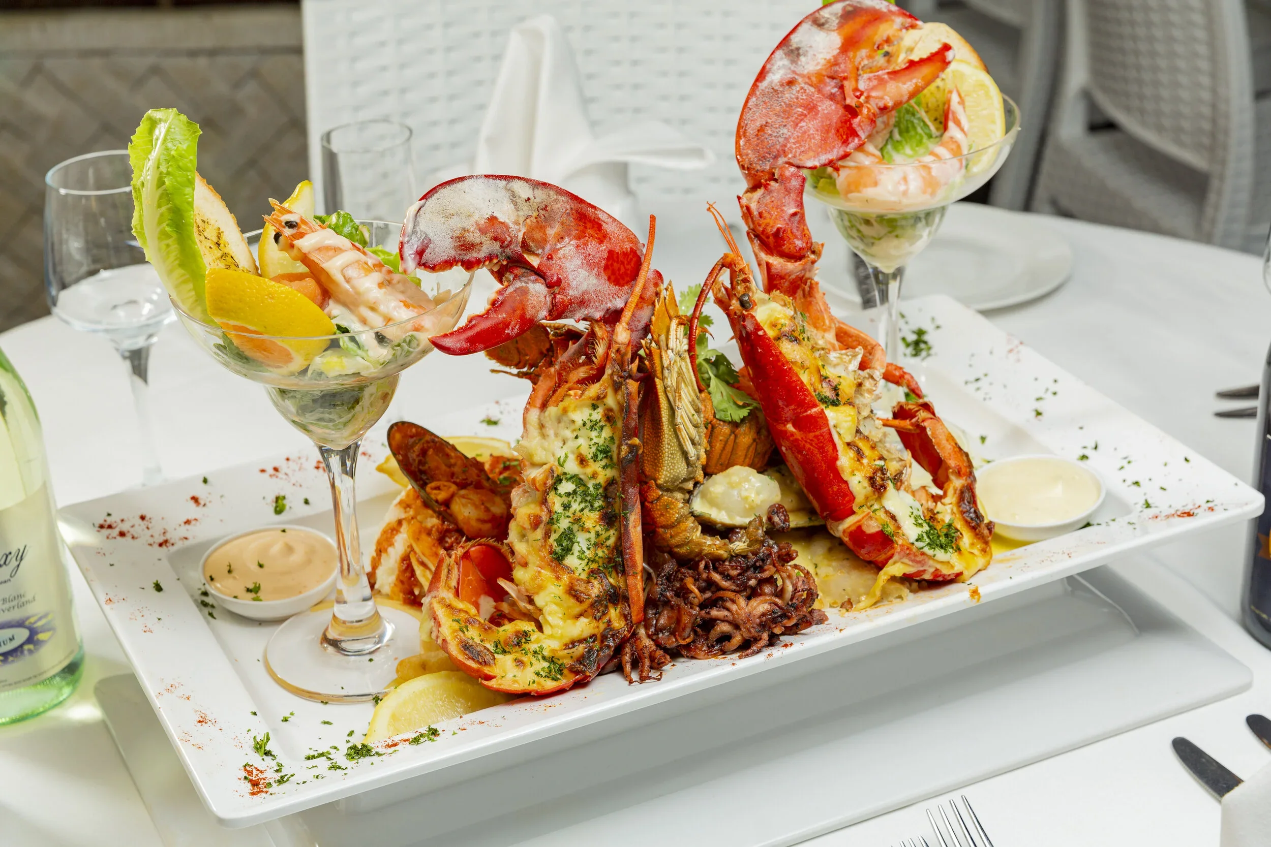 Lobster tail, seafood, and side dishes on a white platter, with garnishes and lemon slices.