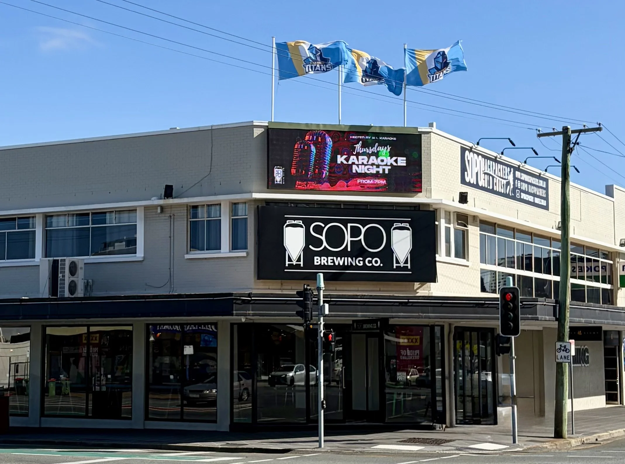 Street front view of SOPO Brewing Company, a large corner establishment high street looking establishment with 3 flags waving above on a sunny day.