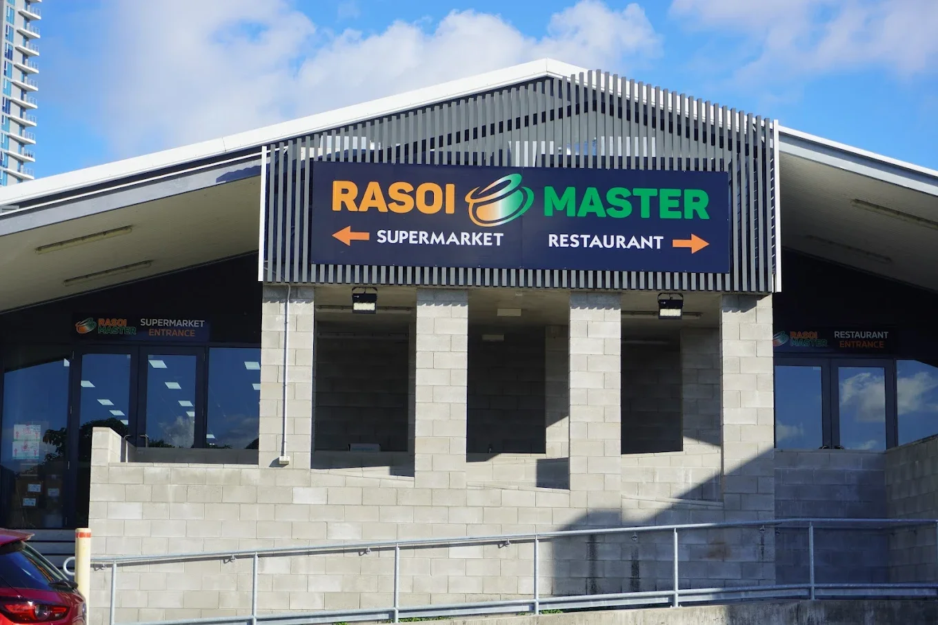 Sign outside a supermarket and restaurant, with arrows pointing left and right, on a building with glass windows and concrete walls.
