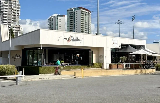 Exterior of Café Catalina with outdoor seating, sun umbrellas, with a patron sitting back turned in a bright blue shirt on a nice day.