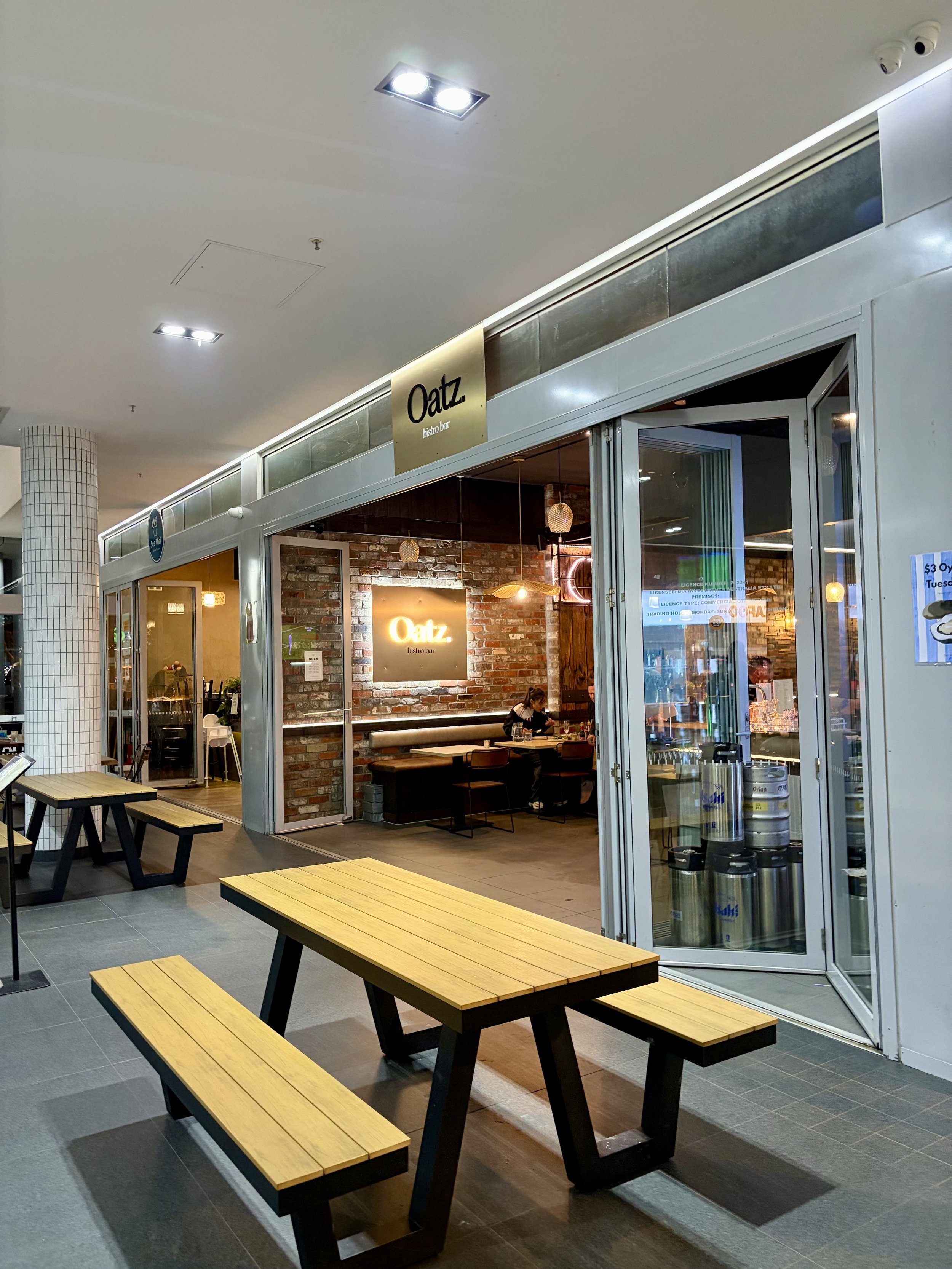 Front view of new Asian fusion restaurant 'Oatz.' in Southport showing tables and bench seats out front and padded booths within and large illuminated Oatz signage.