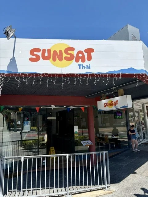 Exterior awning with signage for a restaurant named Sunsat Thai with a white awning and logo in red and yellow.